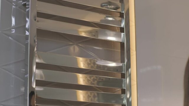 Woman's hands removes white towel from heated towel rail, dryer in bathroom
