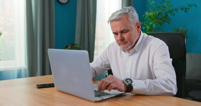 Old middle aged businessman working with laptop, busy senior mature man paying bills online banking managing finances checking budget doing paperwork using computer sitting at desk