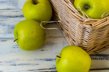 Green apples and basket with apples on wooden background