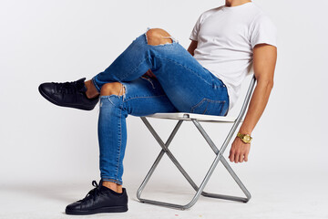 Fototapeta na wymiar a man in jeans and a t-shirt sits on a chair on a light background side view