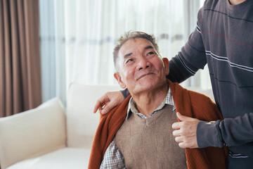 Happy son covering his father with a blanket in their house. Elderly man and happy family.