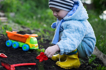 Boy in bright clothes plays on black soil with a toy dump truck