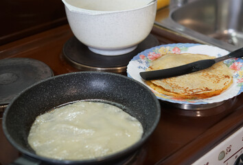 We prepare pancakes in a frying pan at home on an old stove. In a frying pan, batter and a plate of ready-made pancakes.