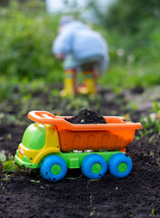 Bright toy dump truck loaded with black soil in the gardens in the spring, in the background a silhouette of a child