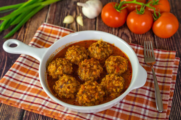 Meatballs with tomato sauce in a frying pan on a wooden table. 