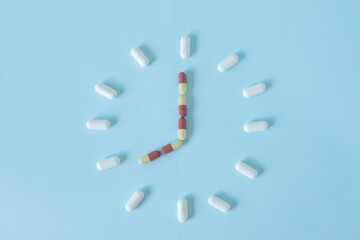 Clock created from white pills on pastel blue background. Right time for using medicines. Period of...