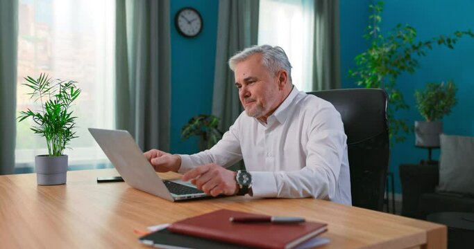 Happy mature 55s man sit at table at home looks at device screen use videocall application on laptop talk with grown up daughter enjoy remote conversation. Modern technology easy comfort usage concept
