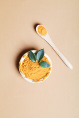 diet nutrition, health care lifestyle concept. Curcuma Longa or turmeric powder in bowl with green leaf and wooden spoon on beige background
