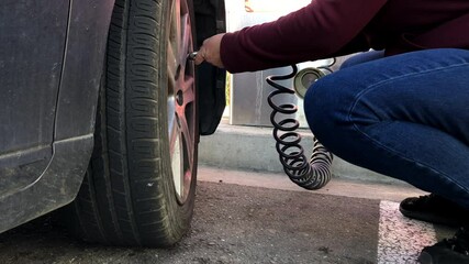 4K HD video of older woman, female hands reaching in to inflate car tire with automated pump at gas station, then replacing tire cap.
