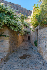 Traditional architecture with narrow stone street and a colorfull bougainvillea in the medieval castle of Monemvasia, Lakonia, Peloponnese, Greece.	