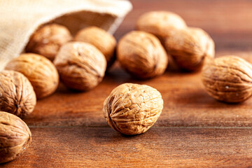 A pile of fresh raw English Walnuts scattered on a wooden table out of burlop vintage  bag. A rustic image  with close up selective focus on walnuts in shell. Angled top view.