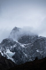 The peak of a mountainf with snow and fog, in a cloudy day