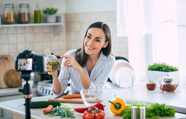 Professional beautiful happy young woman is blogging for her  kitchen channel about healthy living...