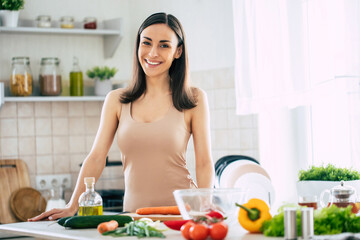 Cute happy young brunette woman in good mood preparing a fresh vegan salad for a healthy life in...
