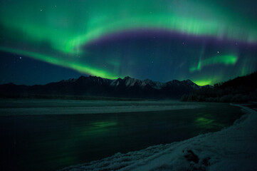 Alaska river with Aurora band over mountains. 