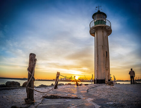 lighthouse in the sunset. Man stay alone on edge and look at the sun.