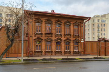 A wooden old house with many beautiful windows with brown carved shutters. Floral pattern, many decorative elements in the decoration. Historic renovated house on Tyumen street (Russia) 