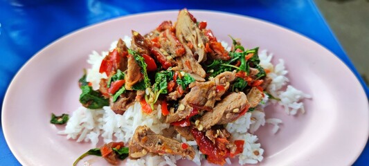 Thai hot and spicy stir fried roasted duck with Thai basil over rice at street food shop.