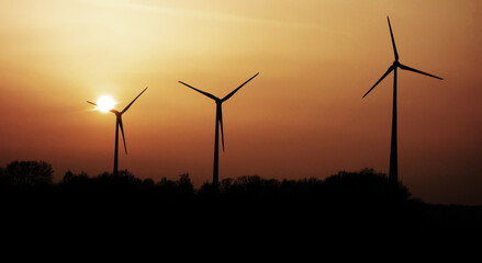 The silhouettes of three wind turbines at sunset.