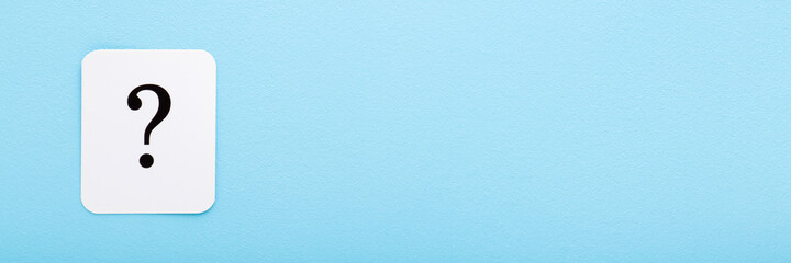 White card of black question mark on light blue table background. Pastel color. Empty place for...