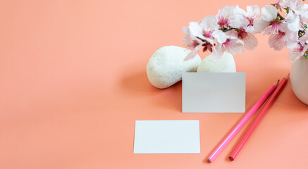 Mockup template of business card, pensils and natural elements on the pink background. Beautiful almond flowers and white stones. Banner photo, space for text or logo or any information.