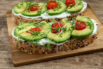 Healthy snacks with microgreens - cereal bread sandwiches with soft cheese, avocado slices, cherri tomatoes and watercress sprouts