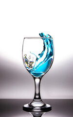 Splashing blue water into the crystal wine glass, closely spreading on a white background.