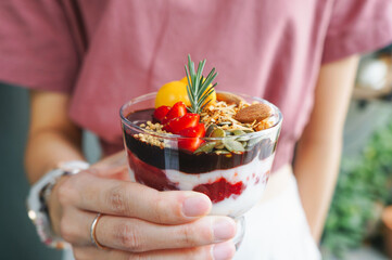 Selective focus Granola and yogurt with berries in jar on a woman hand. Concept of weight loss, fitness food, healthy eating and balanced diet