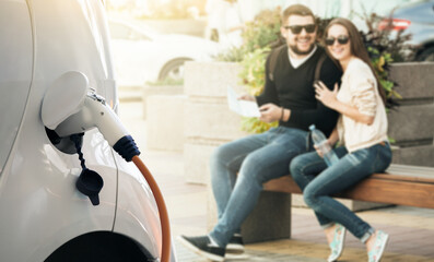 Close up of charging electric car. Smiling couple on a background