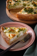A slice of traditional french open quiche pie with feta cheese and broccoli on a dark green background.