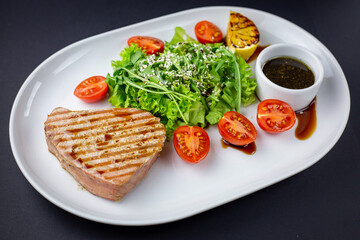 Grilled tuna steak with green salad, tomatoes and soya sauce.