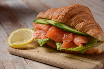 Crispy croissant with salmon and lettuce and cucumbers. Tasty breakfast.