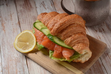 Crispy croissant with salmon and lettuce and cucumbers. Tasty breakfast.