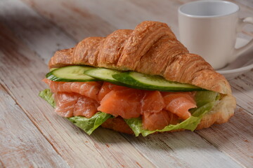 Crispy croissant with salmon and lettuce and cucumbers. Tasty breakfast.