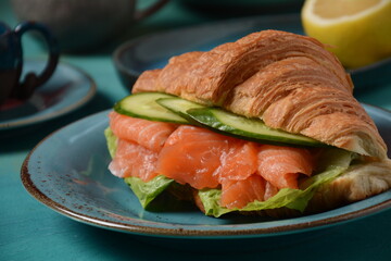 Crispy croissant with salmon and lettuce and cucumbers. Tasty breakfast.