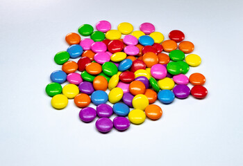 Selective focus of a pile of colorful chocolate buttons on a white paper background.