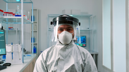 Fototapeta na wymiar Man scientist in ppe suit looking exhausted at camera in modern equipped lab. Overworked team examining virus evolution using high tech and chemistry tools for scientific research, vaccine development