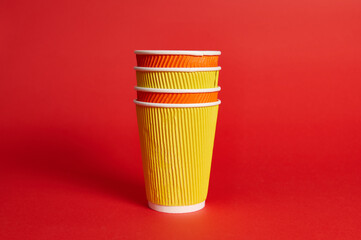 Stack of multicolored paper disposable cups for hot drinks on a red background with copy space.