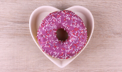 Round pink donut in white heart shaped plate on wooden background