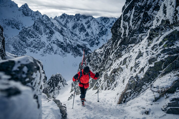 Side view of a male mountain climber going up snowy slope with axes against clouds. Ski tourer...