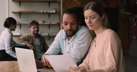 Concentrated young caucasian woman discussing financial paper reports or reviewing marketing research results with skilled male african american colleague, working together in modern coworking office. - Powered by Adobe