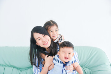 Asian mother sitting with her daughter and son on sofa at home.