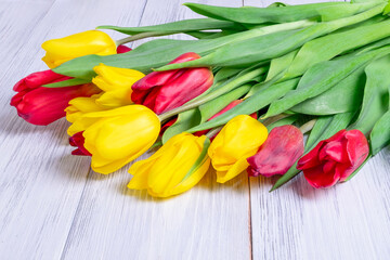 Close-up of a bouquet of yellow and red spring tulips lies on a table with a wooden light surface. Horizontal orientation, selective focus.