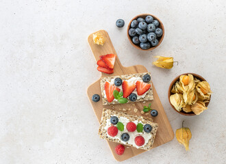 Rye oats crispbread with cottage cheese, mint leaves, fresh strawberries and blueberries. Healthy food snack.