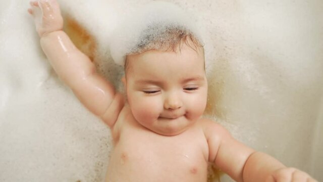 close-up of a little baby girl lying on her back in the bathroom all in foam