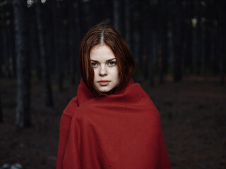 A frozen woman with a red blanket on her shoulders in the forest
