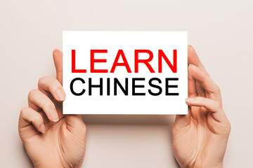 Female hands hold card paper with text Learn Chinese on a yellow background. Education and language concept