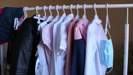 Obraz premium a blue medical mask hangs on a hanger in a women's wardrobe as a necessary accessory for everyday life, children's streetwear on a hanger and a protective mask as part of life in a pandemic