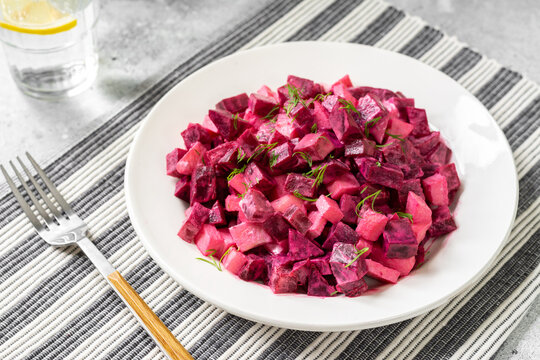 Traditional Scandinavian beetroot and apple salad with mayonnaise, sour cream and balsamic vinegar. Pickled beets with apples in a white plate on a light gray table