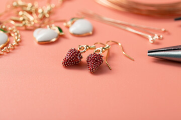 Making jewelry with your own hands at home. Production of earrings from metal accessories and enamel pendants in the form of strawberries. Macro image